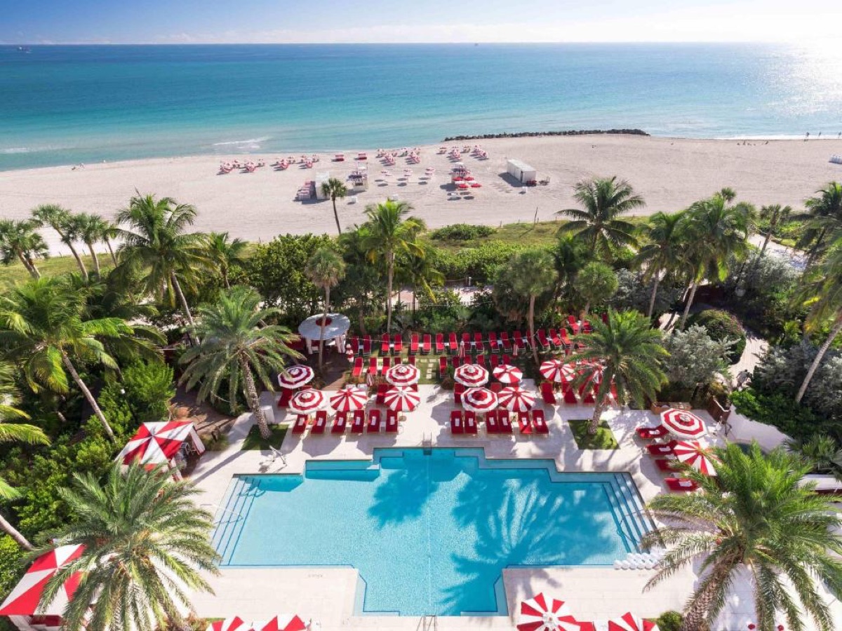 A beachfront hotel pool lined with red and white parasols