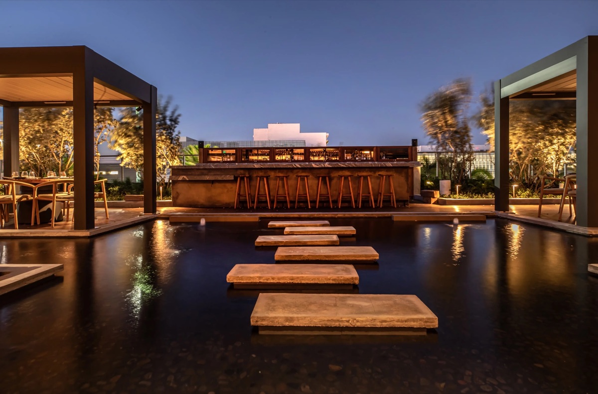 A restaurant terrace and bar at dusk, stepping stones across a reflecting pool
